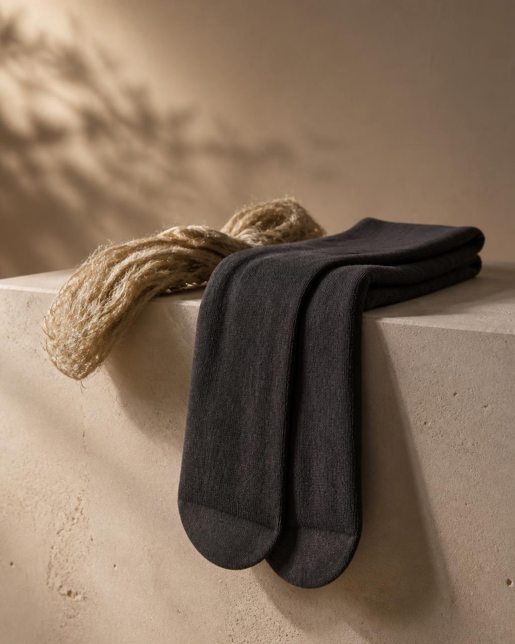 Semi-opaque charcoal hemp stockings folded over a limestone plinth beside raw hemp fiber